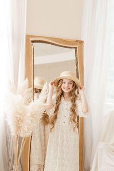 A beautiful teenage girl with long hair measures a straw hat in front of a mirror. Self-admiration of a blonde. selective focus