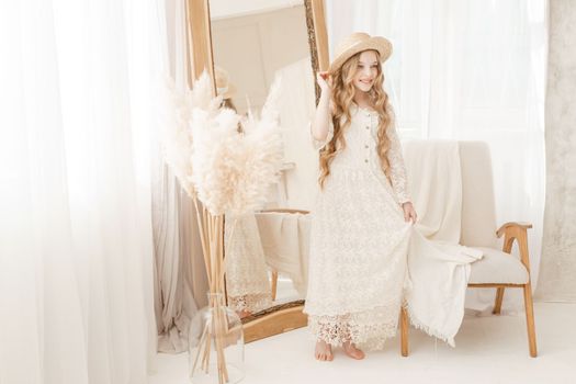 A beautiful teenage girl with long hair measures a straw hat in front of a mirror. Self-admiration of a blonde. selective focus