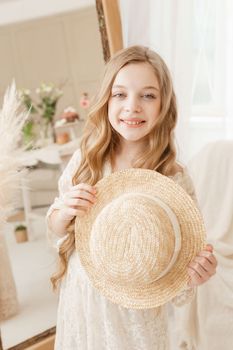 A beautiful teenage girl with long hair measures a straw hat in front of a mirror. Self-admiration of a blonde. selective focus