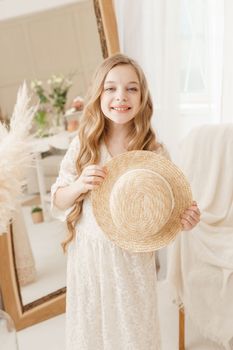 A beautiful teenage girl with long hair measures a straw hat in front of a mirror. Self-admiration of a blonde. selective focus