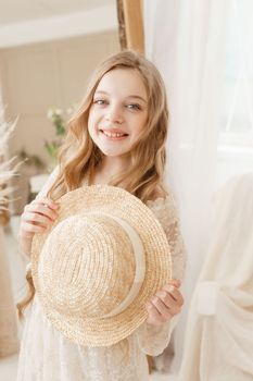A beautiful teenage girl with long hair measures a straw hat in front of a mirror. Self-admiration of a blonde. selective focus