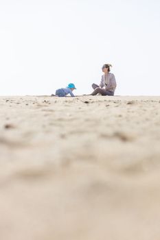 Mother playing his infant baby boy son on sandy beach enjoying summer vacationson on Lanzarote island, Spain. Family travel and vacations concept. Copy space.