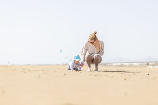 Mother playing his infant baby boy son on sandy beach enjoying summer vacationson on Lanzarote island, Spain. Family travel and vacations concept.