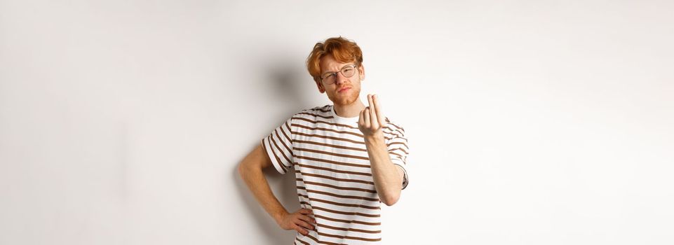 Image of satisfied young man with red hair and glasses showing chefs kiss gesture to praise something perfect, standing over white background.