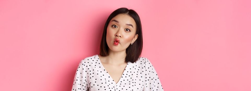 Beauty and lifestyle concept. Close-up of funny and cute asian woman pucker lips, showing fish mouth and standing playful, standing over pink background.