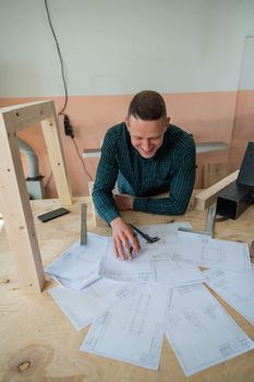 Portrait of a carpenter in a plaid shirt draws a workshop blueprint