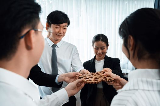 Closeup hand holding wooden gear by businesspeople wearing suit for harmony synergy in office workplace concept. Group of people hand making chain of gears into collective form for unity symbol.