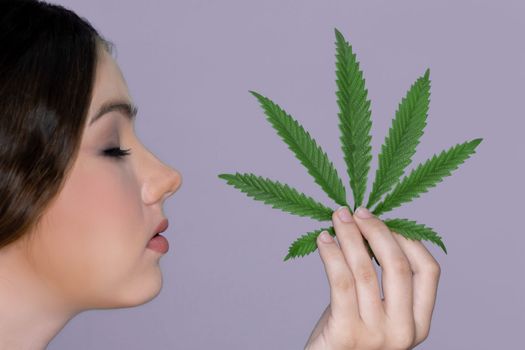 Closeup charming girl with fresh skin hold green leaf for beauty skin care made from cannabis leaf. Cosmetology and cannabis concept with isolated background. Woman holding cbd leaf side view.
