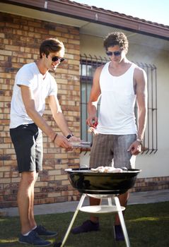 Barbequing it to perfection. Young guys barbecuing meat on the grill outdoors - Lifestyle