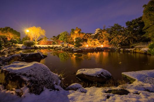 Lamp light on pond in snow-covered Japanese garden at dawn. High quality photo