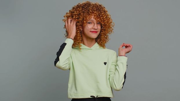 Cheerful lovely young child girl kid in glasses smiling looking at camera. Funny female teenager children schoolgirl with curly frizzy hair isolated portrait alone on studio gray background. Childhood