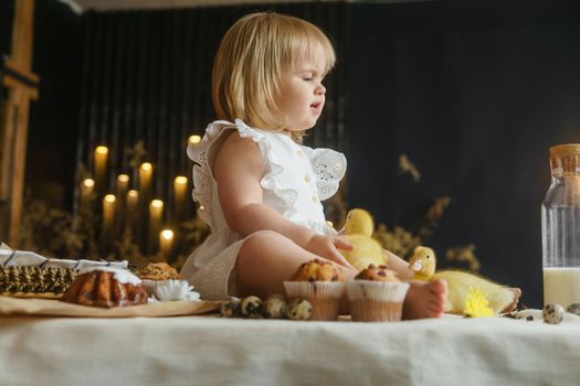 A little girl is sitting on the Easter table and playing with cute fluffy ducklings. The concept of celebrating happy Easter