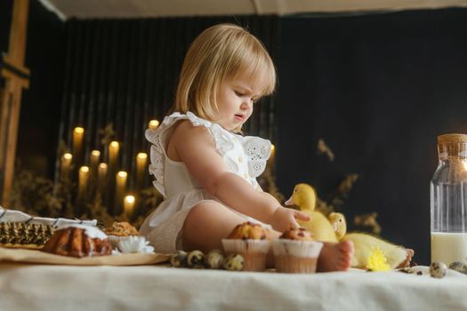 A little girl is sitting on the Easter table and playing with cute fluffy ducklings. The concept of celebrating happy Easter