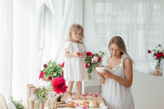 A little blonde girl with her mom on a kitchen countertop decorated with peonies. The concept of the relationship between mother and daughter. Spring atmosphere.