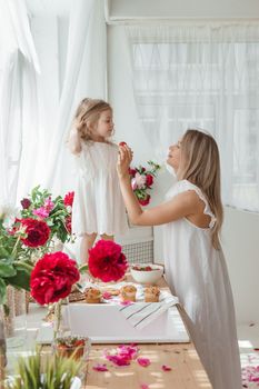 A little blonde girl with her mom on a kitchen countertop decorated with peonies. The concept of the relationship between mother and daughter. Spring atmosphere.