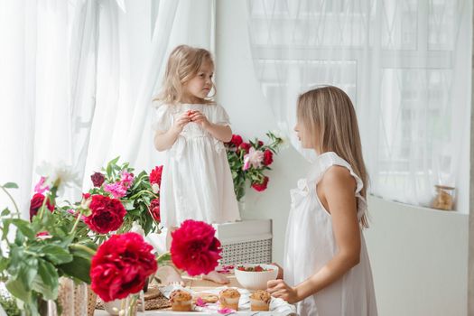 A little blonde girl with her mom on a kitchen countertop decorated with peonies. The concept of the relationship between mother and daughter. Spring atmosphere.