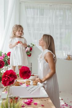 A little blonde girl with her mom on a kitchen countertop decorated with peonies. The concept of the relationship between mother and daughter. Spring atmosphere.