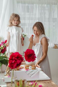 A little blonde girl with her mom on a kitchen countertop decorated with peonies. The concept of the relationship between mother and daughter. Spring atmosphere.