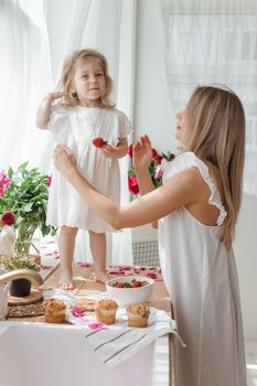 A little blonde girl with her mom on a kitchen countertop decorated with peonies. The concept of the relationship between mother and daughter. Spring atmosphere.