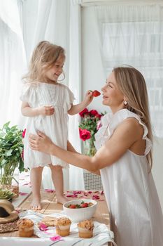 A little blonde girl with her mom on a kitchen countertop decorated with peonies. The concept of the relationship between mother and daughter. Spring atmosphere.