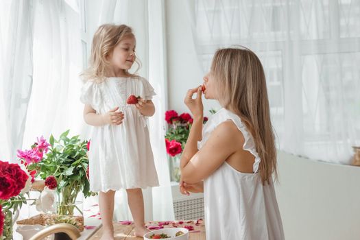 A little blonde girl with her mom on a kitchen countertop decorated with peonies. The concept of the relationship between mother and daughter. Spring atmosphere.