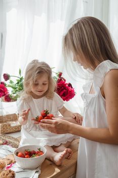 A little blonde girl with her mom on a kitchen countertop decorated with peonies. The concept of the relationship between mother and daughter. Spring atmosphere.