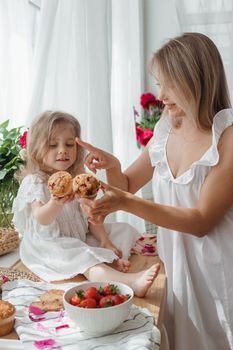 A little blonde girl with her mom on a kitchen countertop decorated with peonies. The concept of the relationship between mother and daughter. Spring atmosphere.