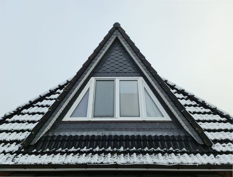 Open roof window in velux style with black roof tiles covered in snow
