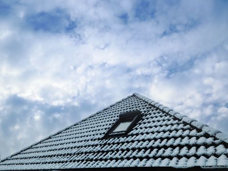 Open roof window in velux style with black roof tiles covered in snow