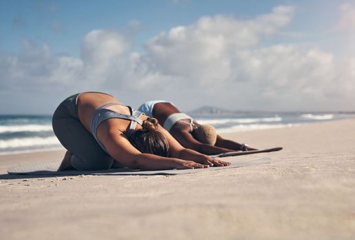 Yoga keeps us physically and mentally fit. two young women practicing yoga on the beach
