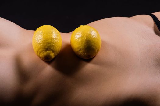 Young woman with cellulite problem and lemon on a dark background, closeup