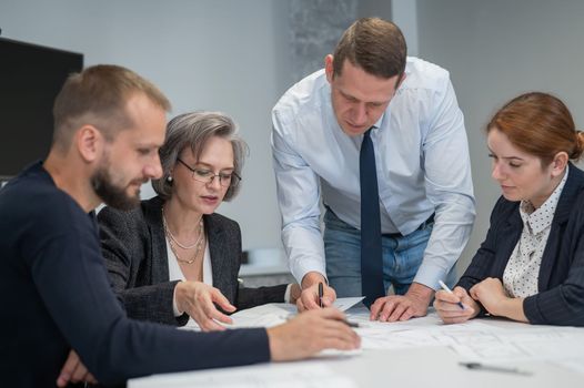 Four colleagues are discussing blueprints in a conference room in an office. Brainstorming of engineers and architects