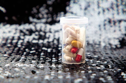 Transparent bottle of assorted natural supplement, on a black sequin background