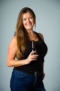 Isolated portrait of a forty year old woman wearing a black tank top, holding a brown bottle of beer