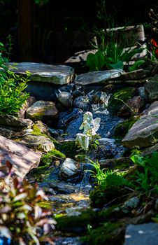 White statue of a faerie playing the flute, sitting in a stream