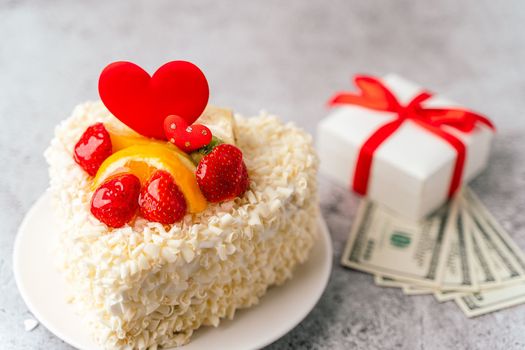 Valentine's Day cake, money dollars bills, gift with heart shape and fruits, strawberries. Birthday Cake for celebration. Valentine's Day and love concept. Present with love.