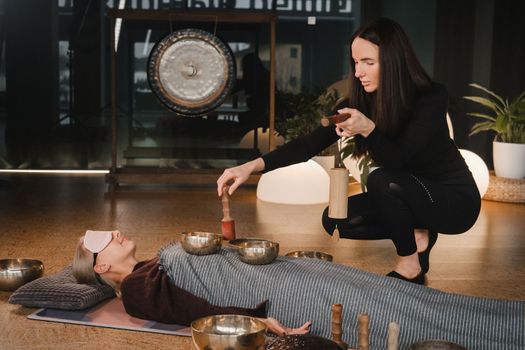 A young beautiful woman is doing a massage with singing bowls and a koshi bell to another girl. Sound therapy.