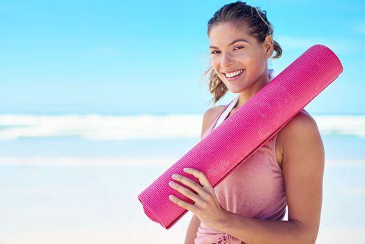 It doesnt have to be yoga OR the beach. a young woman holding a yoga mat while standing on the beach