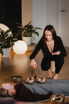 A young beautiful woman is doing a massage with singing bowls and a koshi bell to another girl. Sound therapy.