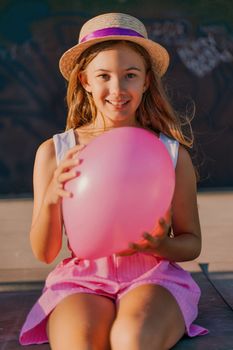 Portrait of a girl in a hat with a pink balloon. She is dressed in pink clothes and her hair is long and loose