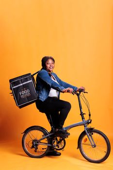 Restaurant courier holding thermal backpack ready to deliver take away meal to client using bike. Pizzeria worker carrying bag while delivering fast food meal, takeout service and transportation