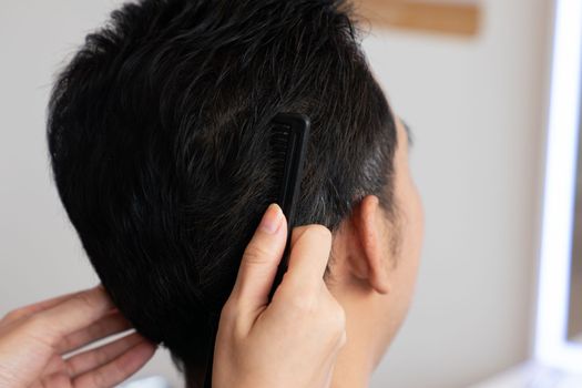 Closeup asian female barber making haircut for male customer with male hairstyle in qualified barbershop. Men's hairstyling by a scissor and comb in hair salon concept.