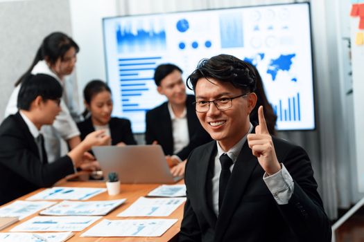 Focus portrait of successful confident male manager or executive in business wear with blurred background of businesspeople, colleagues working with financial report papers in office of harmony.
