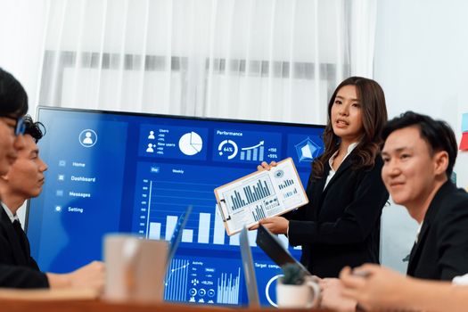Confidence and young asian businesswoman give presentation on financial business strategy in dashboard report display on screen to colleagues in conference room meeting as harmony in workplace concept