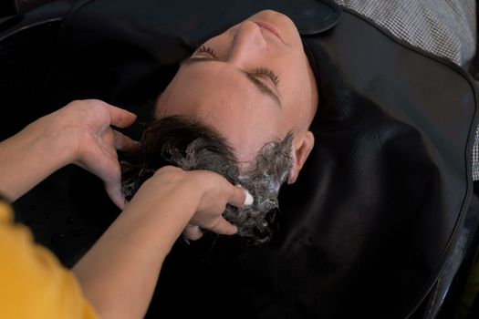 Closeup caucasian man getting hair wash by professional hairdresser with shampoo feels relax and comfortable . Qualified hairdresser with her barbershop, salon providing haircare concept.