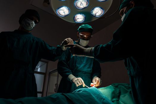 Surgical team performing surgery to patient in sterile operating room. In a surgery room lit by a lamp, a professional and confident surgical team provides medical care to an unconscious patient.