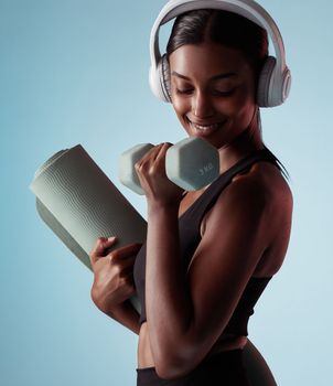 Yoga, dumbbell and woman in studio training strong biceps in exercise with headphones for music streaming. Fitness, healthy and happy girl listening to audio, radio and lifting weights for arm power.