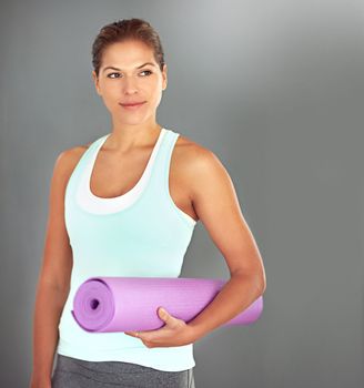 Looking forward to her yoga session. a young woman holding a yoga mat while standing against a gray background
