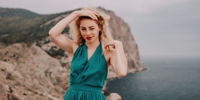 Side view a Young beautiful sensual woman in a mint long dress posing on a volcanic rock high above the sea during sunset. Girl on the nature on overcast sky background. Fashion photo