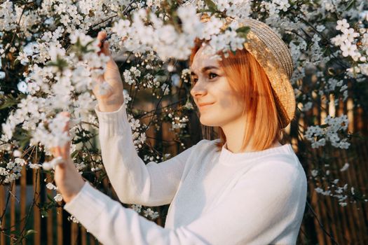 Portrait of a woman in a straw hat in a cherry blossom. Free outdoor recreation, spring blooming garden